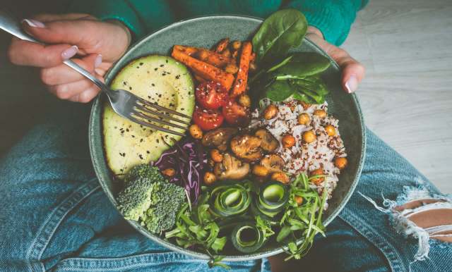 A bowl of mixed vegetables, quinoa, and chickpeas held by a person with a fork.