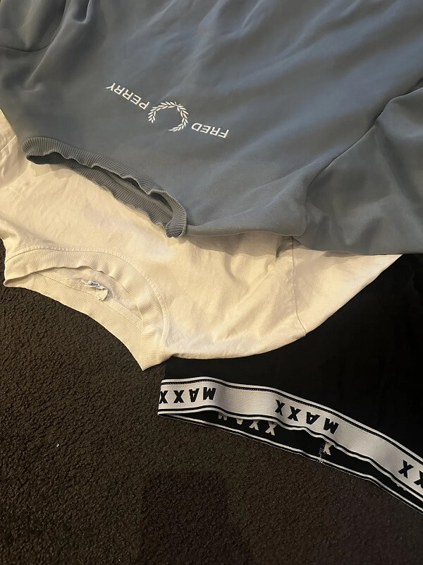 A stack of three clothing items: a gray top, a white T-shirt, and black shorts with a patterned waistband.