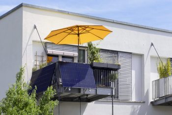 A modern balcony featuring solar panels and a bright yellow umbrella, surrounded by greenery.