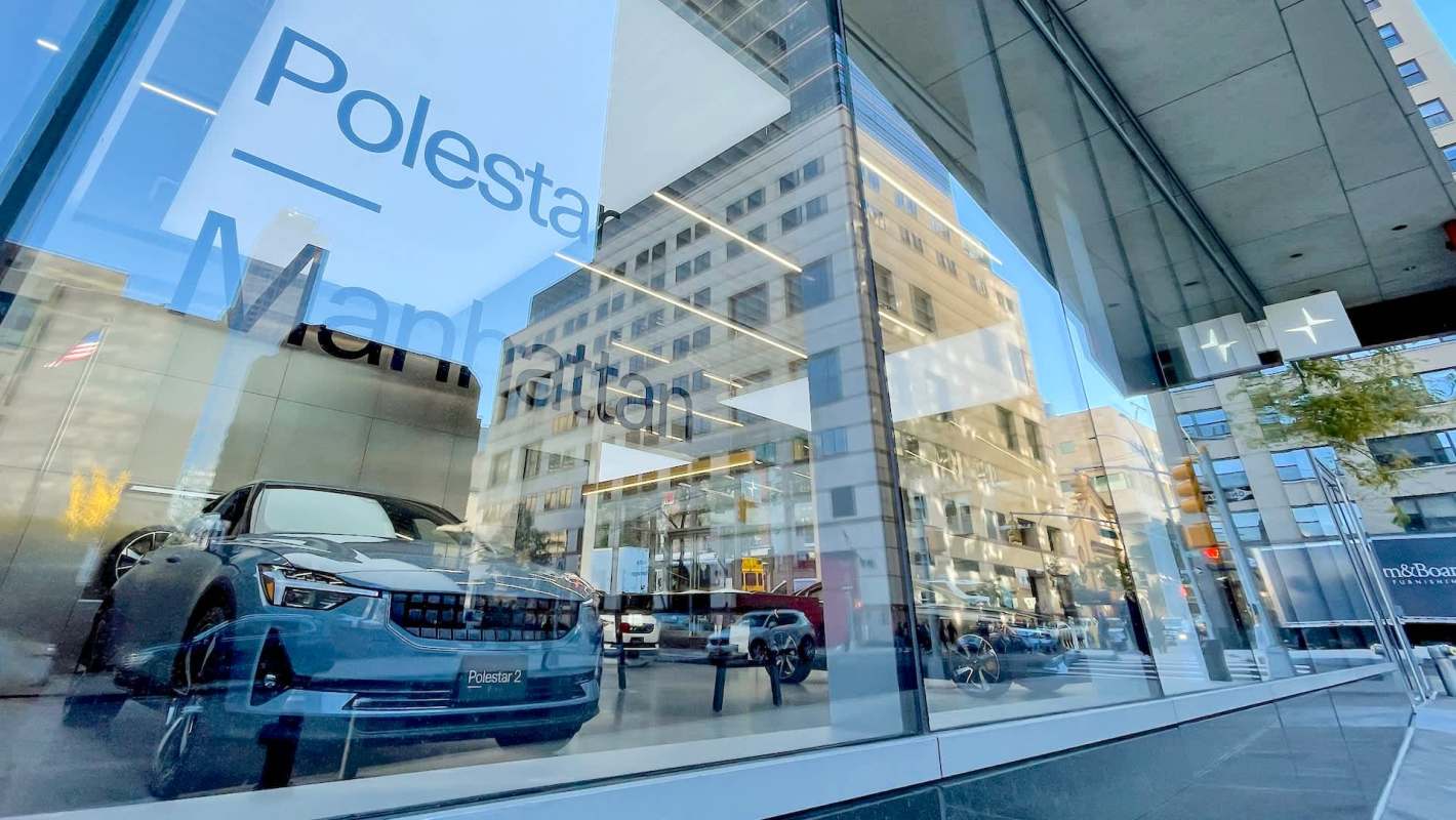 A Polestar 2 car is displayed in a sleek showroom window in Manhattan, reflecting surrounding buildings.