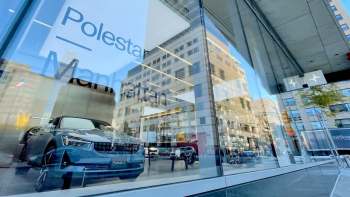 A Polestar 2 car is displayed in a sleek showroom window in Manhattan, reflecting surrounding buildings.