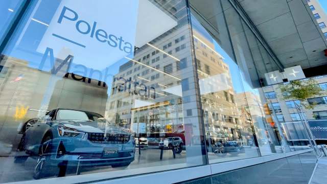 A Polestar 2 car is displayed in a sleek showroom window in Manhattan, reflecting surrounding buildings.