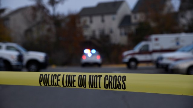 A police line marked "DO NOT CROSS" is set up with emergency vehicles visible in the background.