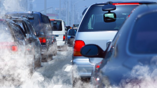 A congested roadway filled with cars, with visible exhaust fumes rising in the air.