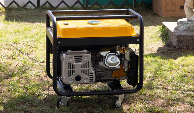 A portable generator with a bright yellow top and black frame, positioned on grass in a backyard setting.