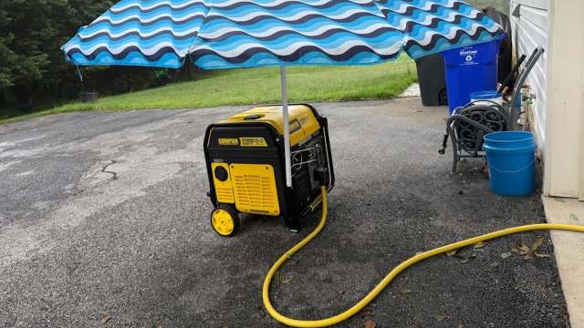 A generator covered by a blue and white striped umbrella on a gravel surface.