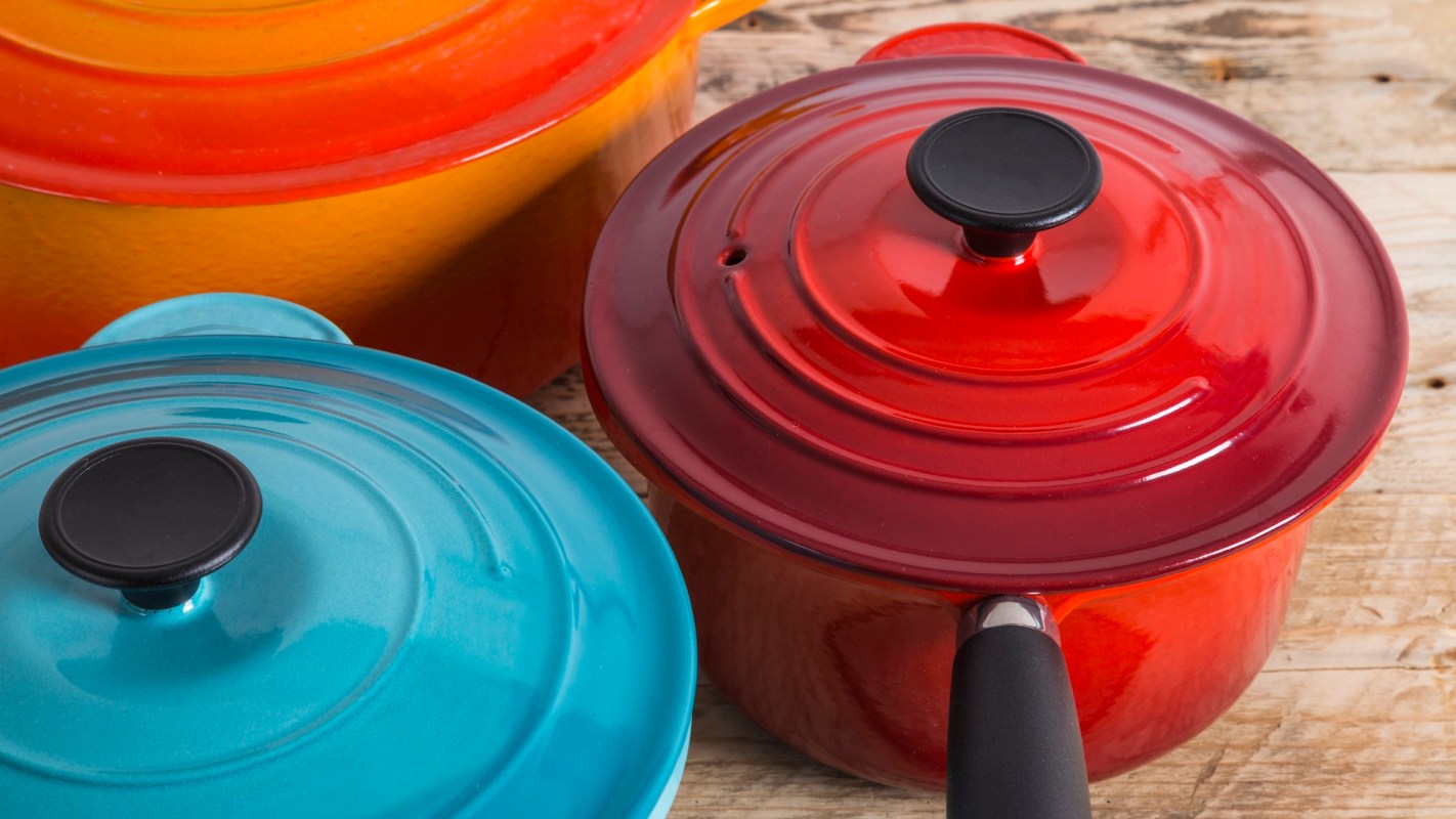 Three colorful cooking pots in teal, red, and orange sit on a wooden surface.