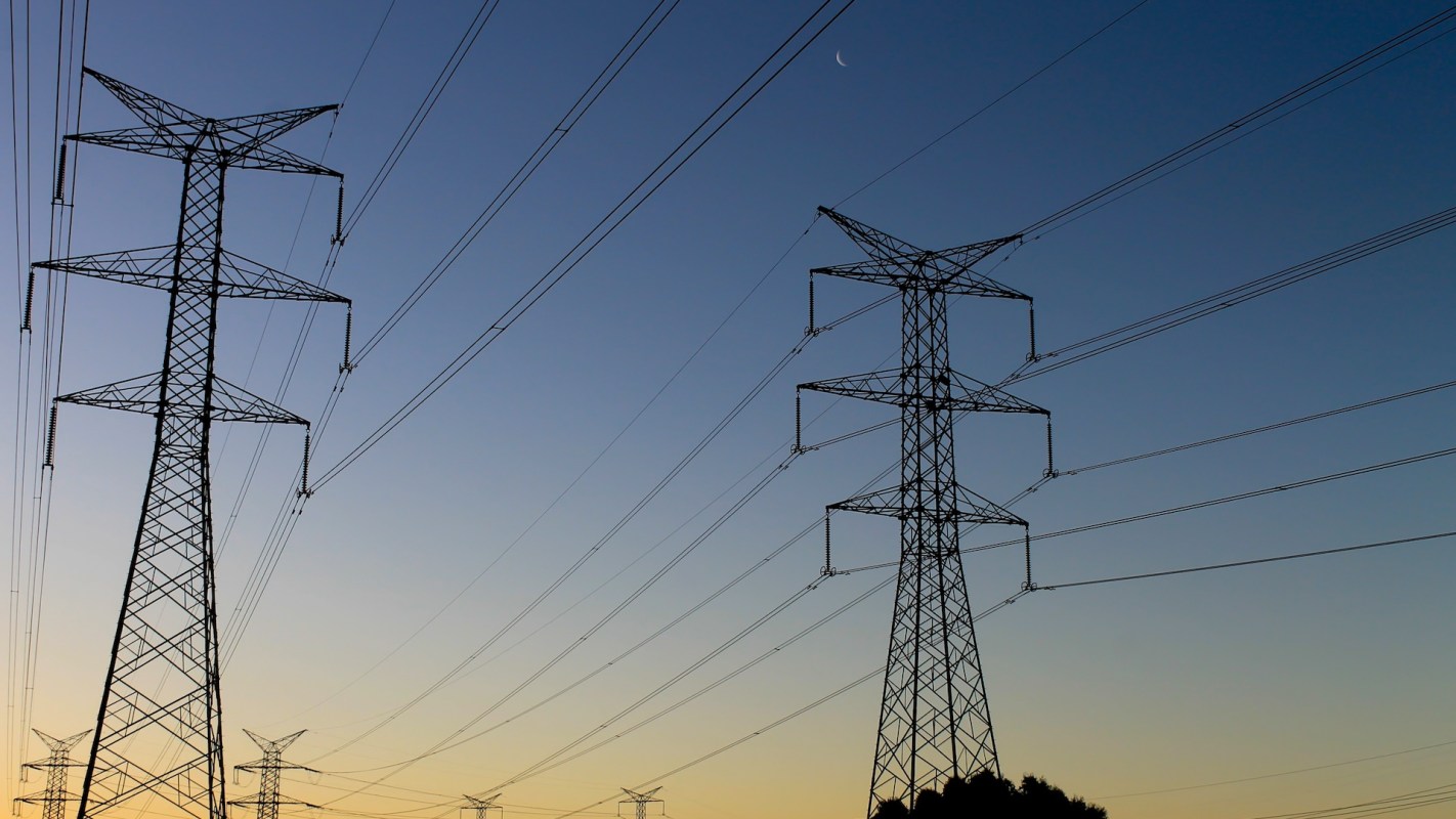 Silhouettes of tall power lines and towers against a twilight sky with a crescent moon visible.