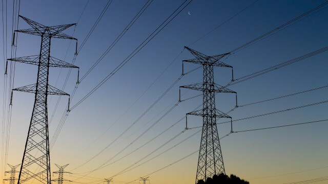 Silhouettes of tall power lines and towers against a twilight sky with a crescent moon visible.