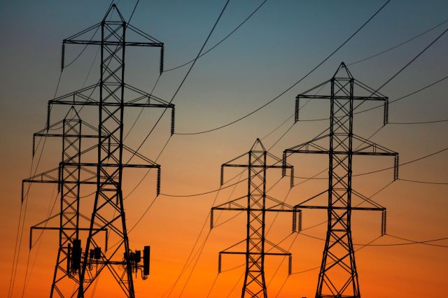 Silhouettes of power lines and transmission towers against a colorful sunset sky.