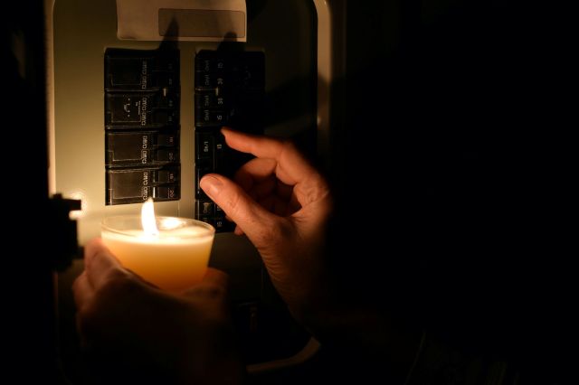 A hand illuminating a circuit breaker with a candle.