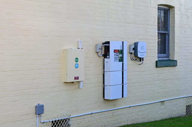 A wall-mounted electrical setup with various boxes and a window in a yellow brick exterior.