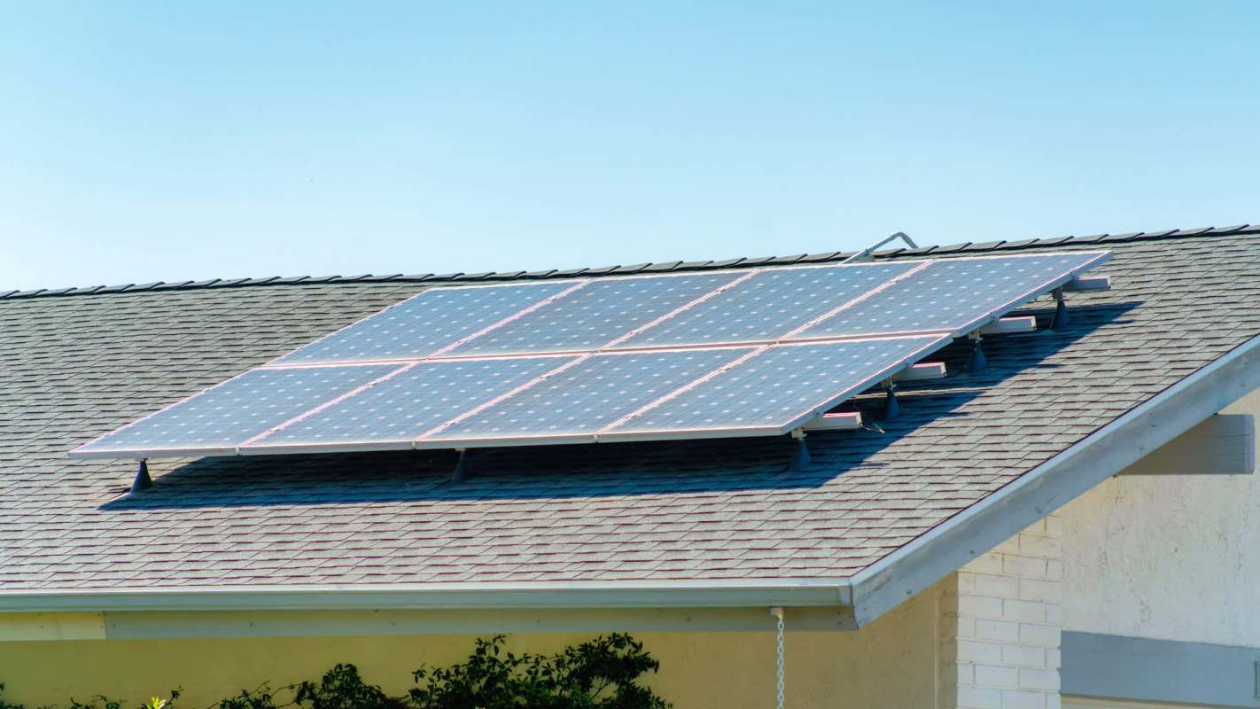 A rooftop solar panel array installed on a sloped roof under a clear blue sky.