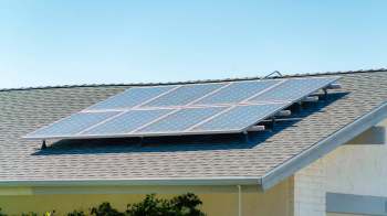 A rooftop solar panel array installed on a sloped roof under a clear blue sky.
