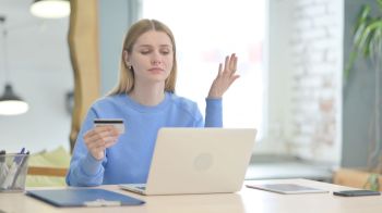 A frustrated woman holding a credit card and using a laptop.