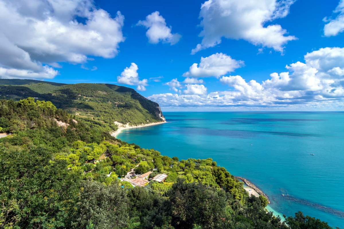 A panoramic view of a coastal landscape with lush greenery and a clear blue sea under a bright sky.