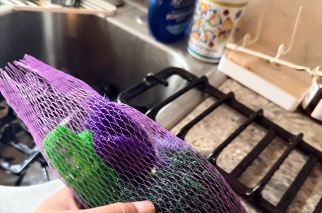 A hand holding a bag of colorful cleaning sponges near a kitchen sink with a visible stove grate.