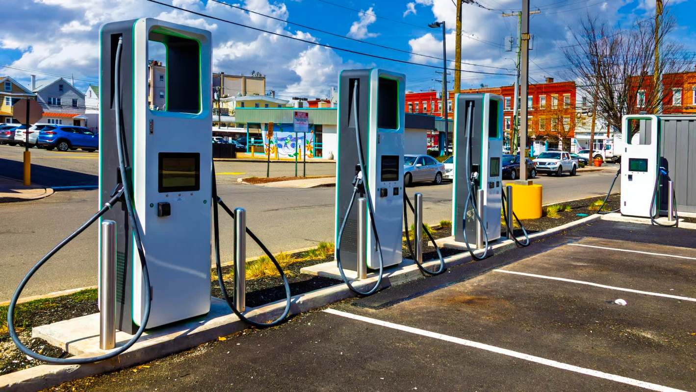 Multiple electric vehicle charging stations lined up in a parking lot under a clear blue sky.