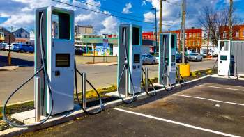 Multiple electric vehicle charging stations lined up in a parking lot under a clear blue sky.