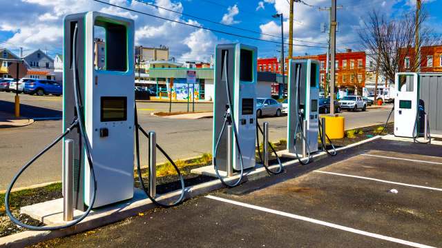 Multiple electric vehicle charging stations lined up in a parking lot under a clear blue sky.