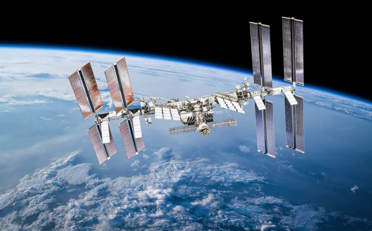 The International Space Station orbits Earth against a backdrop of space and clouds.