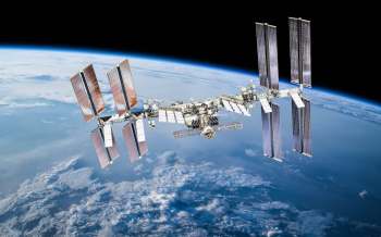 The International Space Station orbits Earth against a backdrop of space and clouds.