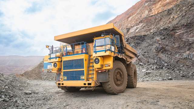 A large yellow dump truck in a mining area surrounded by rocks and earth.