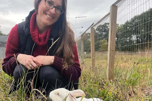 Mallory Cormier kneeling in a field behind a white rabbit.