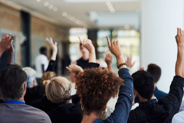 A group of people in an audience raising their hands.