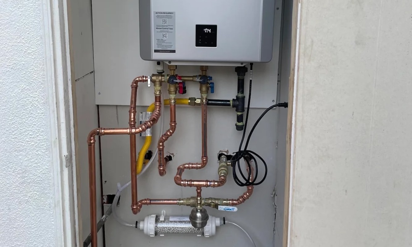 A close-up of a tankless water heating system with copper pipes and a digital control panel inside a utility closet.