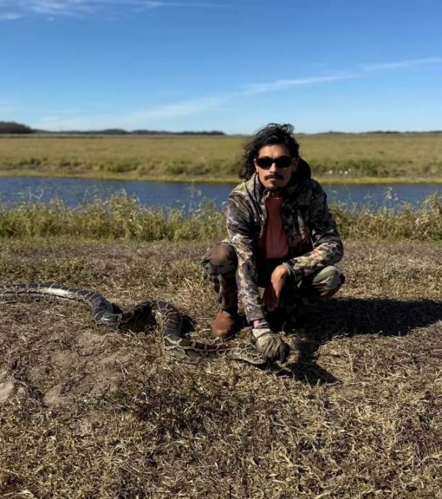 A person kneeling beside a large python.