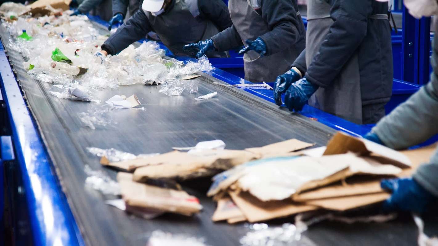 Workers sorting recyclable materials on a conveyor belt in a recycling facility.