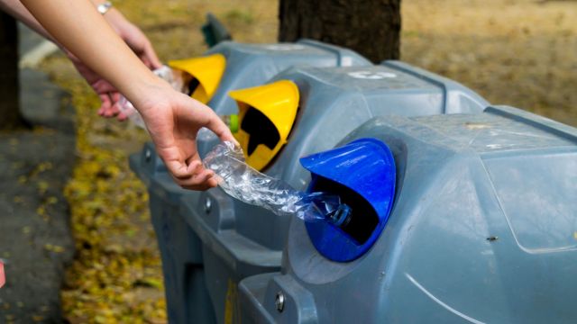A person putting a plastic bottle in a recycling bin.