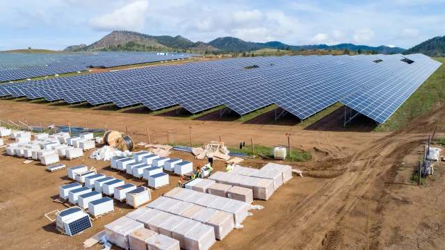 A solar farm with rows of panels and equipment displayed on a dirt field under a blue sky.