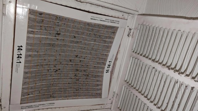 A dirty air filter with a grid pattern, mounted in a ventilation system.