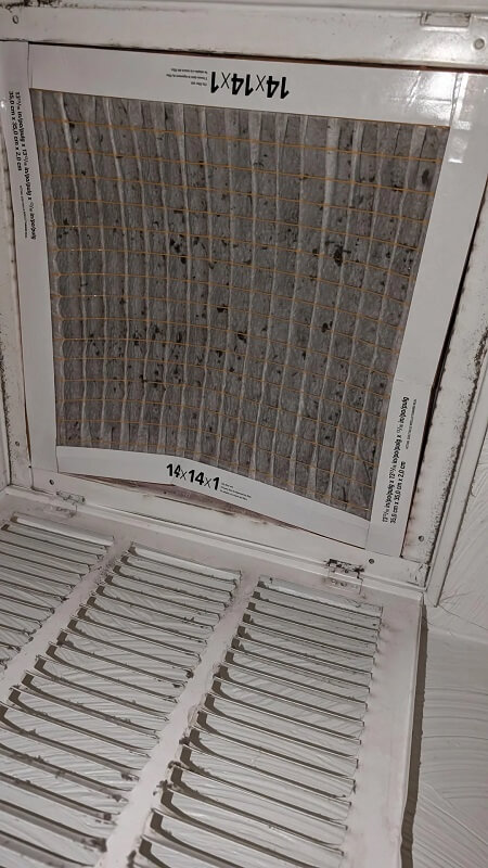A dirty air filter with a grid pattern, mounted in a ventilation system.