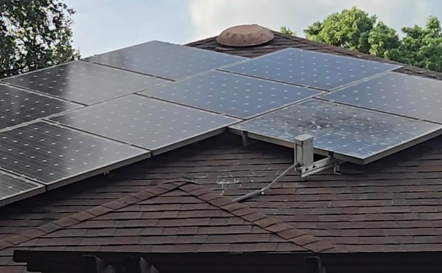 Solar panels installed on a sloped roof with foliage and a cloudy sky in the background.