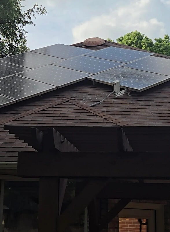 Solar panels installed on a sloped roof with foliage and a cloudy sky in the background.