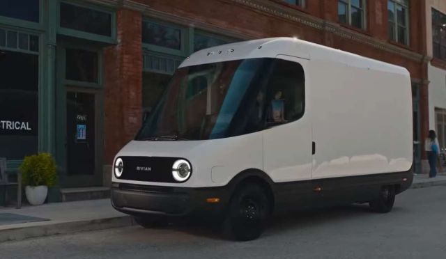 A white Rivian delivery van parked on a city street near brick buildings and pedestrians.
