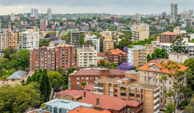 A cityscape view featuring a mix of residential buildings and green trees under a cloudy sky.
