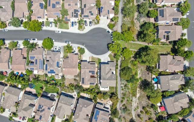 An aerial view of a suburban neighborhood with houses, many with solar panels on their roofs.