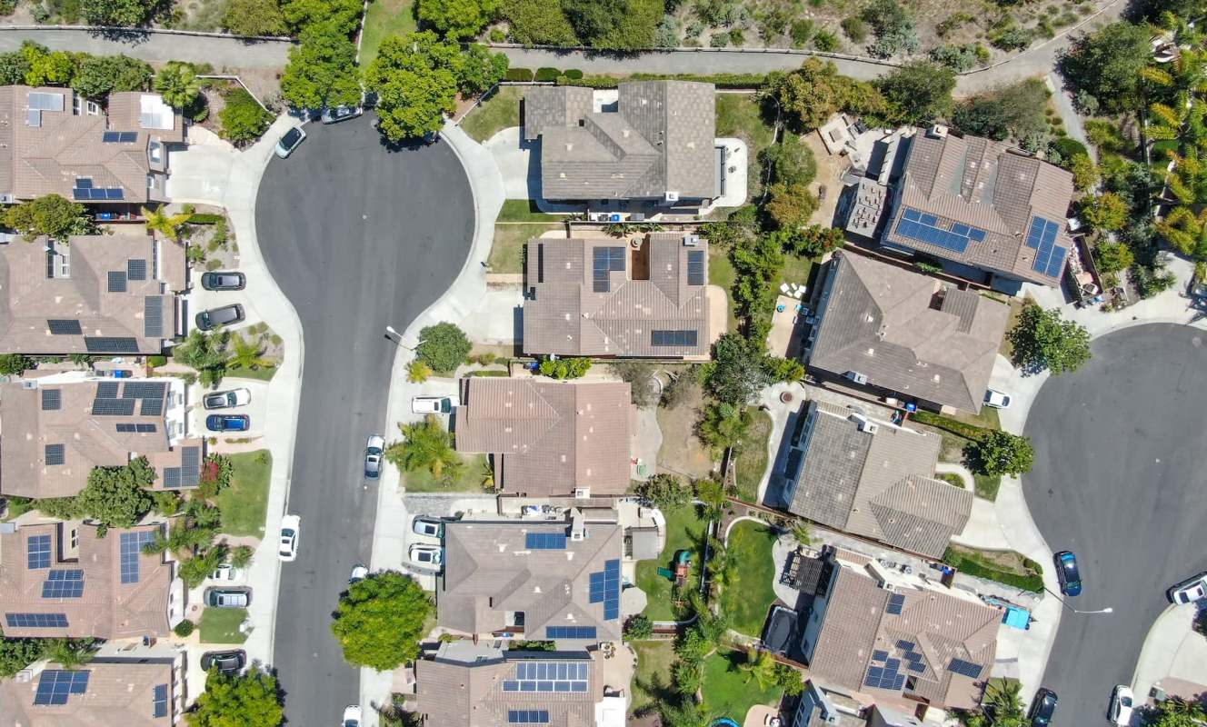 An aerial view of a suburban neighborhood featuring homes with solar panels and a circular street layout.