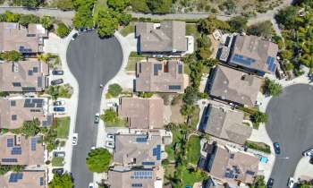 An aerial view of a suburban neighborhood featuring homes with solar panels and a circular street layout.