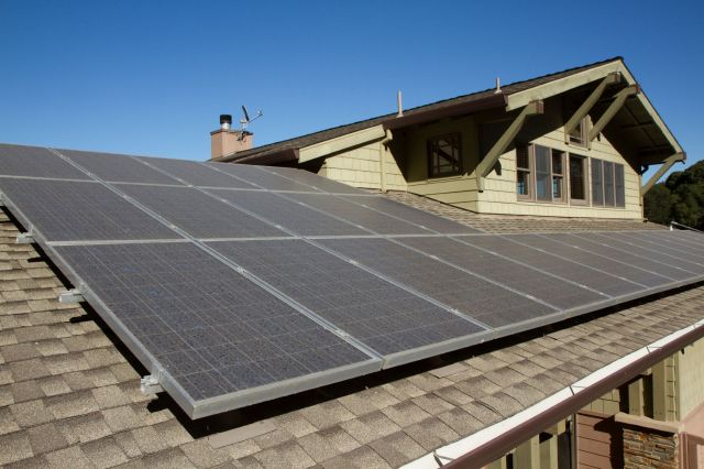A row of solar panels on a grassy field under a partly cloudy sky.