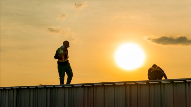 Two workers on a roof at sunset.