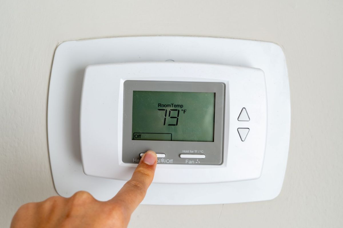 A hand adjusts a digital thermostat displaying a room temperature of 79°F.