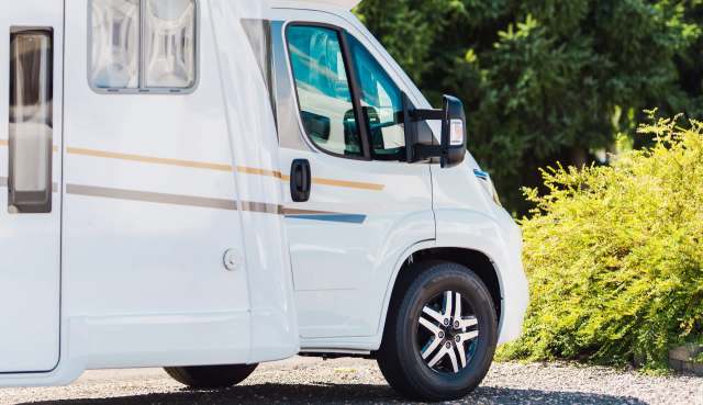 A white camper van parked beside green shrubs with sunlight reflecting off its windows.