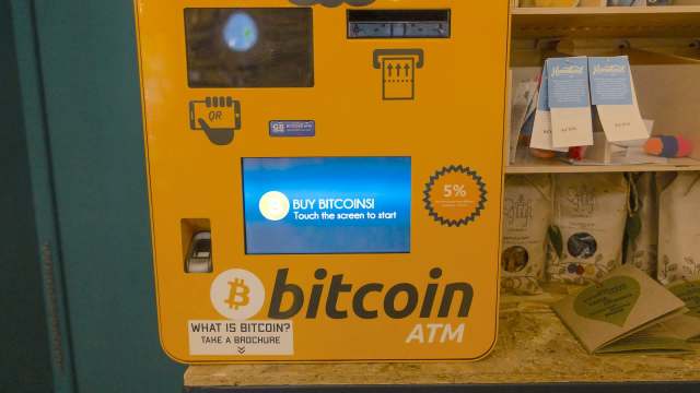 A bright yellow Bitcoin ATM with a touchscreen displaying "BUY BITCOINS! Touch the screen to start."