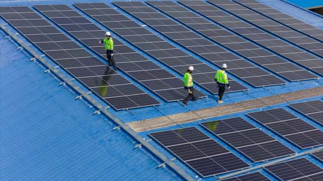 Three workers in hard hats walk on a rooftop covered with solar panels.