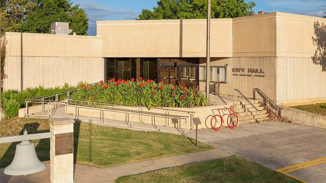 A modern city hall building featuring vibrant flowers, bike racks, and a wheelchair-accessible ramp.
